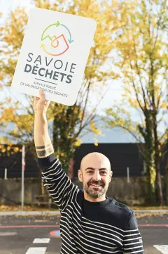responsable communication tenant le logo savoie d&eacute;chets en hauteur sur le parking du centre de tri